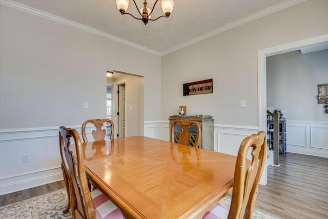 dining room with an inviting chandelier, crown molding, light wood-type flooring, and wainscoting