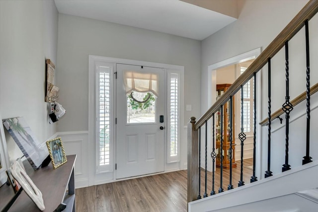 foyer with a decorative wall, stairs, a wainscoted wall, and wood finished floors