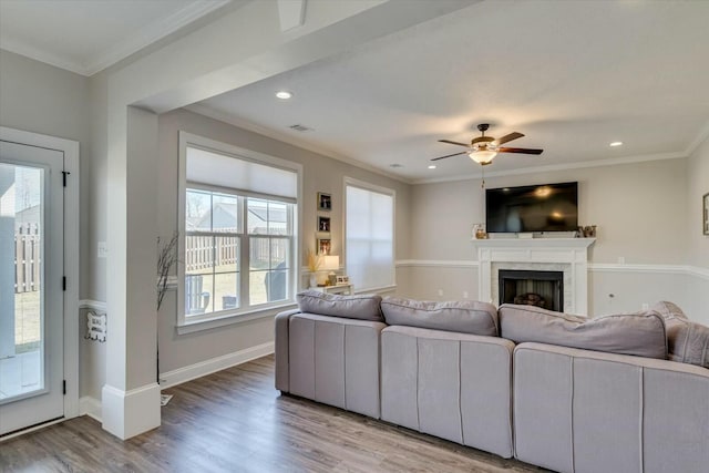 living area with light wood-style flooring, a fireplace, baseboards, and ornamental molding