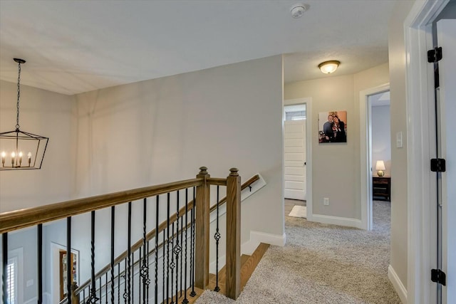 hall featuring baseboards, an upstairs landing, a chandelier, and carpet flooring