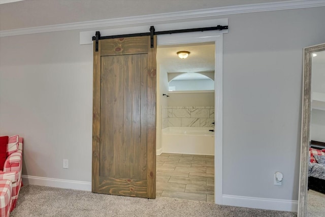 interior space featuring a barn door, baseboards, ensuite bath, and ornamental molding