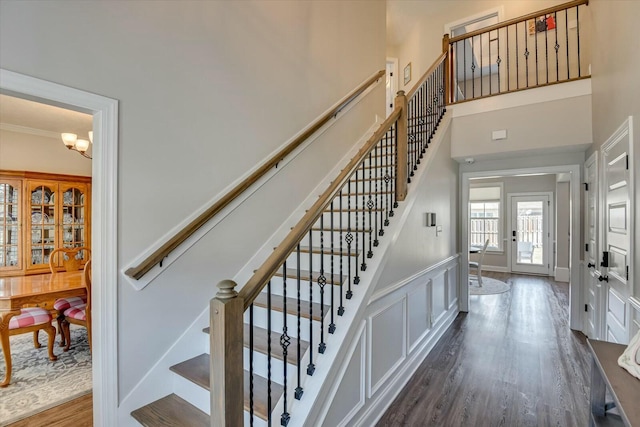 stairway featuring wood finished floors, baseboards, a towering ceiling, crown molding, and a notable chandelier