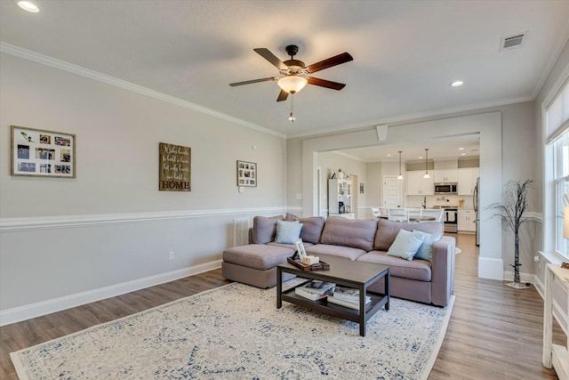 living area with visible vents, light wood-type flooring, crown molding, and baseboards