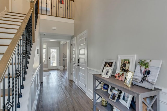 entryway featuring a wainscoted wall, stairway, wood finished floors, and a high ceiling