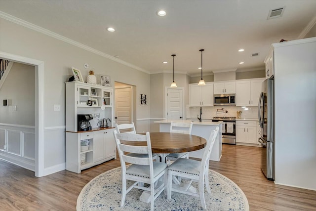 dining area with light wood finished floors, visible vents, and ornamental molding