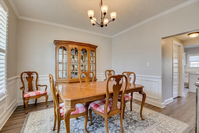 dining space with a chandelier, a wainscoted wall, wood finished floors, and crown molding