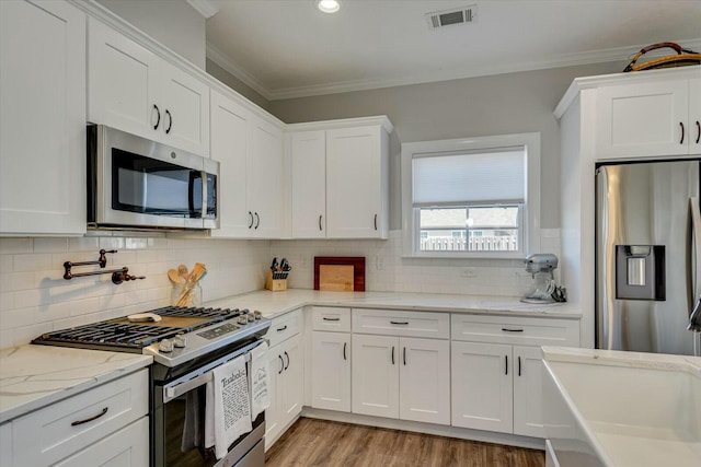 kitchen with visible vents, backsplash, appliances with stainless steel finishes, white cabinets, and crown molding