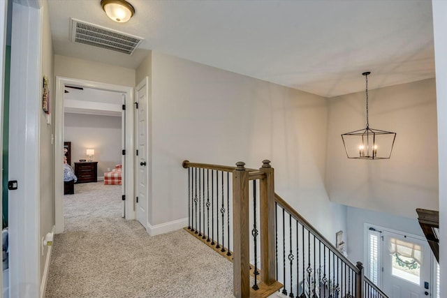 hallway featuring visible vents, baseboards, carpet, a chandelier, and an upstairs landing