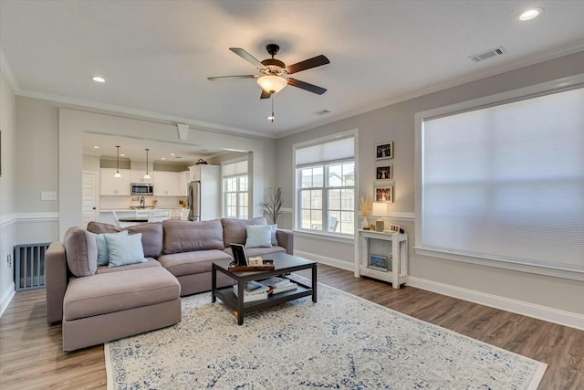 living room with visible vents, ornamental molding, light wood-style flooring, baseboards, and ceiling fan