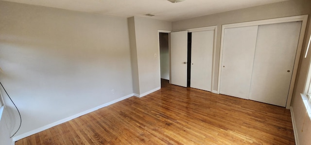 unfurnished bedroom with two closets and hardwood / wood-style flooring