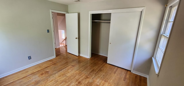 unfurnished bedroom featuring multiple windows, light hardwood / wood-style flooring, and a closet