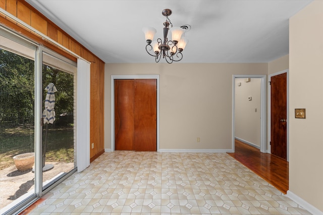 spare room featuring a wealth of natural light, wood walls, and a notable chandelier