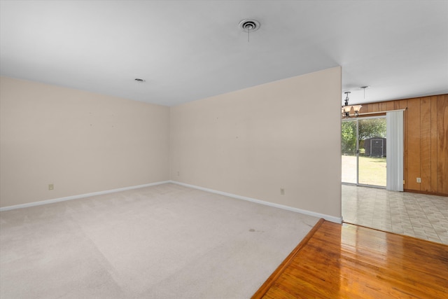 carpeted spare room with a notable chandelier and wood walls