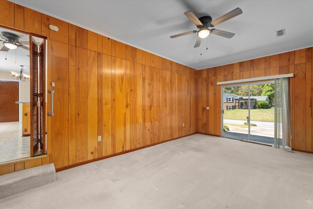 carpeted spare room with wooden walls and ceiling fan with notable chandelier