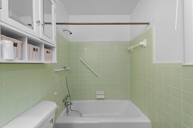 bathroom with tiled shower / bath combo, toilet, and tile walls