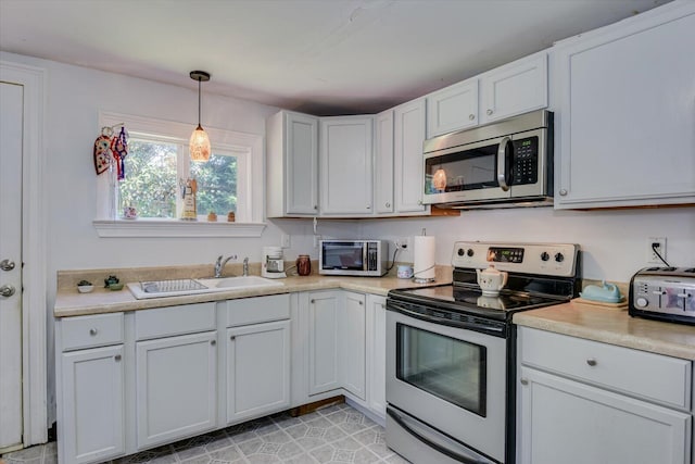 kitchen with white cabinets, sink, light tile patterned floors, appliances with stainless steel finishes, and decorative light fixtures