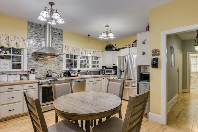 kitchen featuring decorative backsplash, appliances with stainless steel finishes, a notable chandelier, and wall chimney range hood