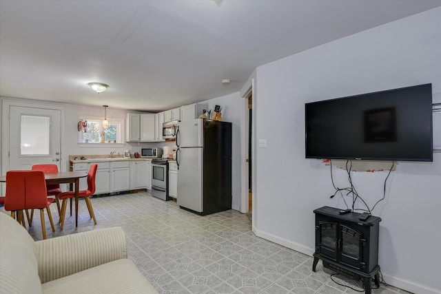 kitchen with pendant lighting, stainless steel appliances, white cabinetry, and a wood stove