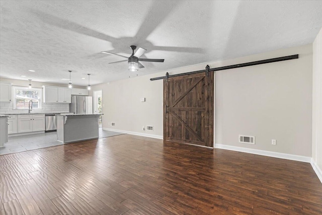 unfurnished living room with wood finished floors, visible vents, a sink, ceiling fan, and a barn door