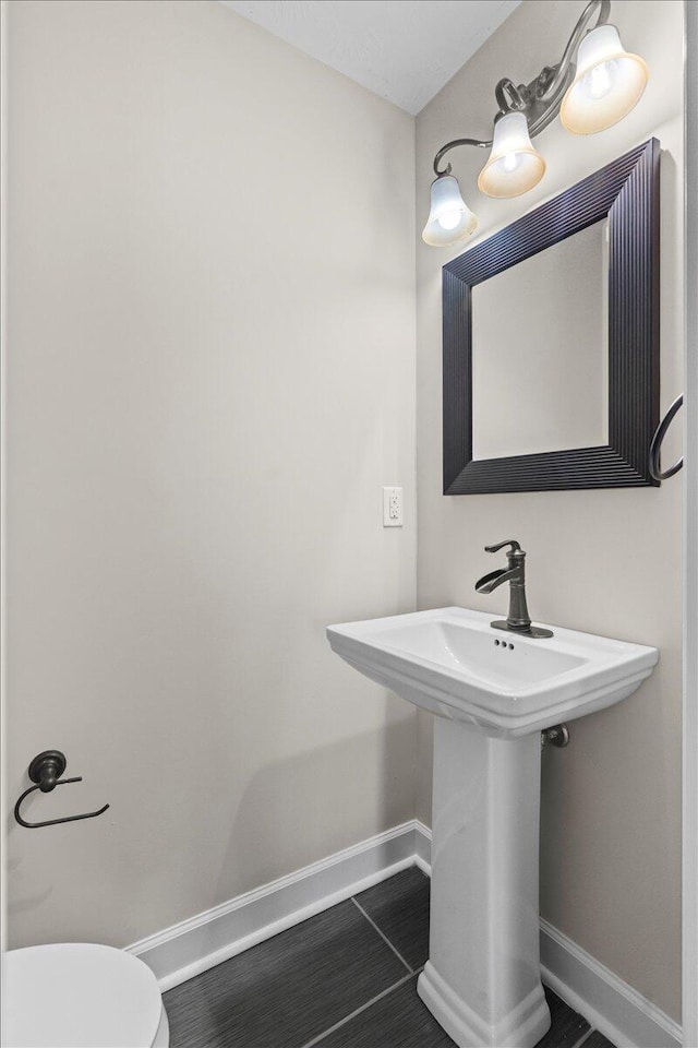 half bathroom featuring tile patterned floors, toilet, baseboards, and a sink