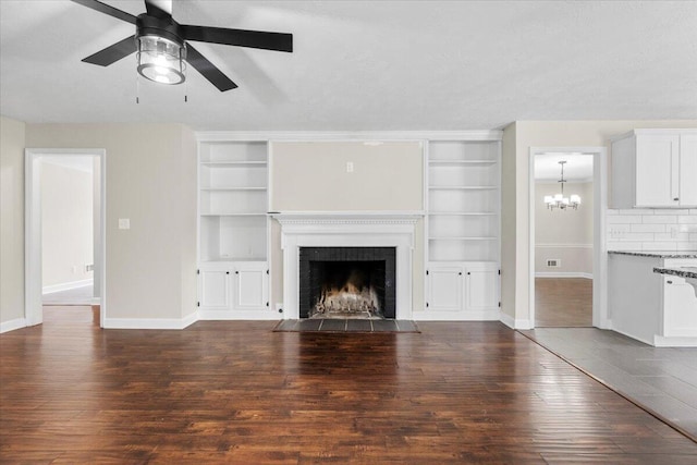 unfurnished living room with baseboards, a fireplace with flush hearth, dark wood finished floors, and ceiling fan with notable chandelier