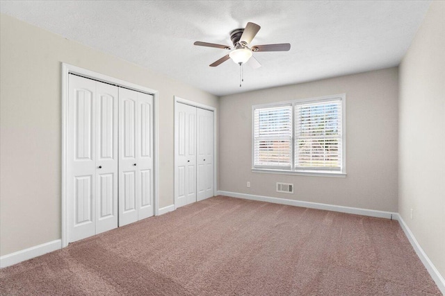 unfurnished bedroom with baseboards, visible vents, two closets, and carpet