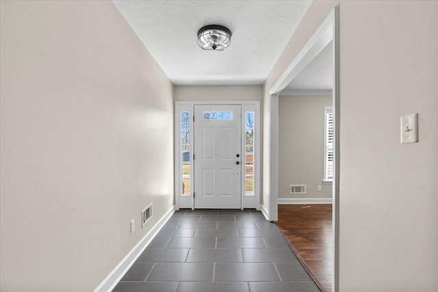 foyer entrance featuring baseboards, visible vents, dark wood-style flooring, and a textured ceiling