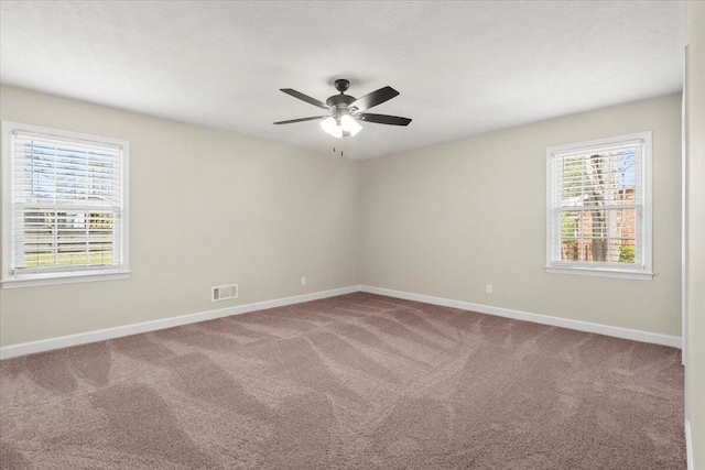 carpeted empty room with baseboards, visible vents, and ceiling fan