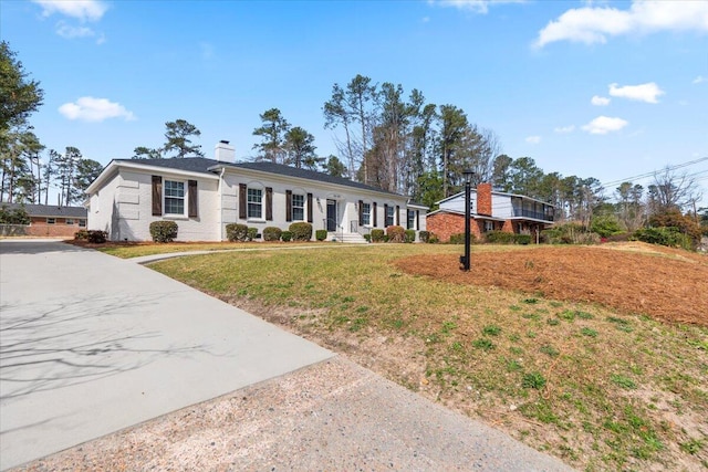 ranch-style house with a front yard, a chimney, and driveway