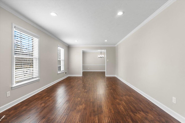 empty room with dark wood finished floors, crown molding, a notable chandelier, and baseboards