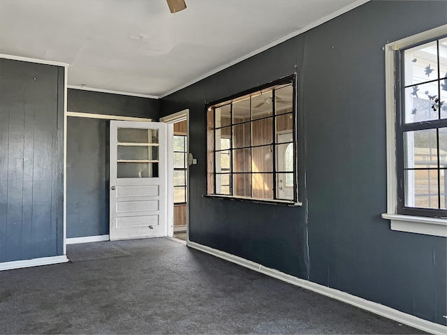 empty room featuring dark carpet, ceiling fan, crown molding, and a wealth of natural light