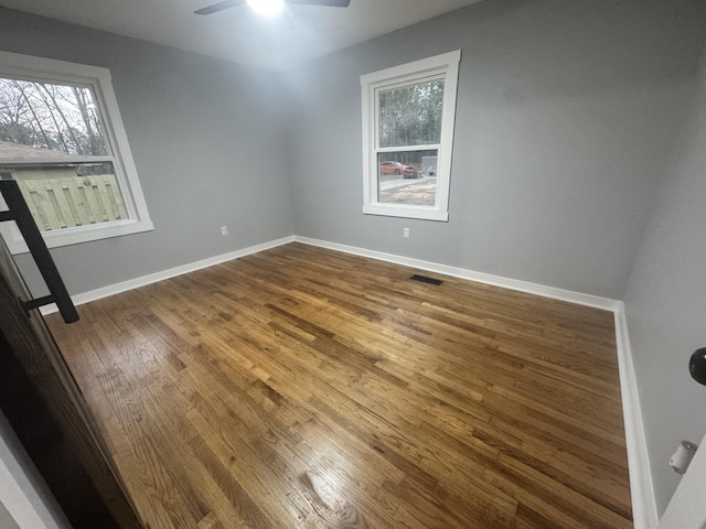 spare room with visible vents, wood finished floors, a ceiling fan, and baseboards