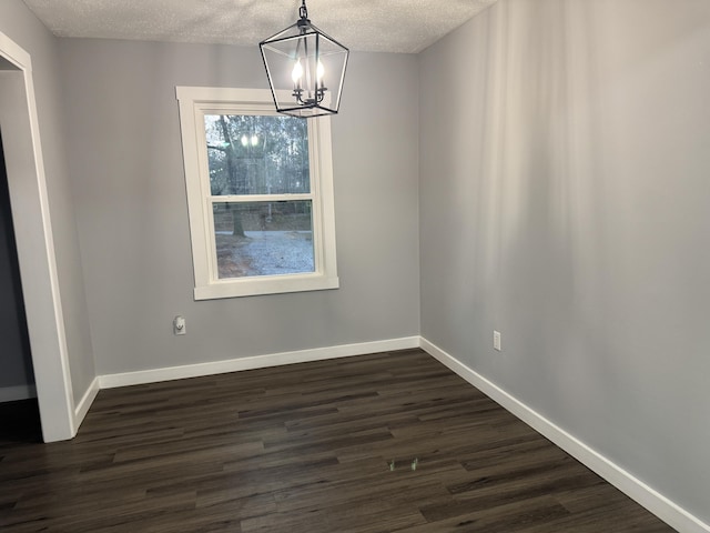 unfurnished dining area featuring a textured ceiling, dark wood-style flooring, a notable chandelier, and baseboards