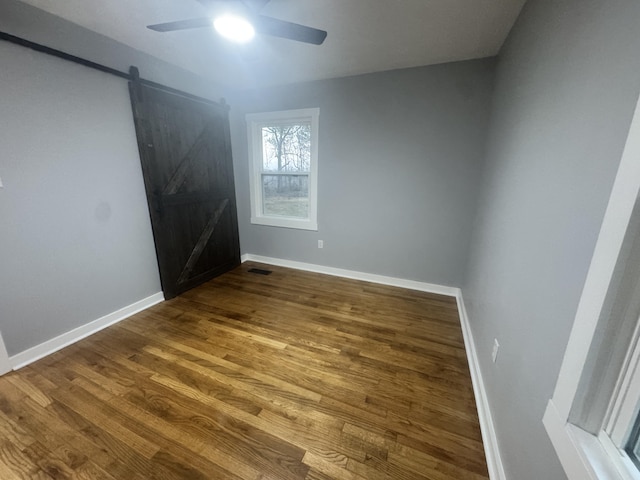 empty room with a ceiling fan, wood finished floors, baseboards, and a barn door