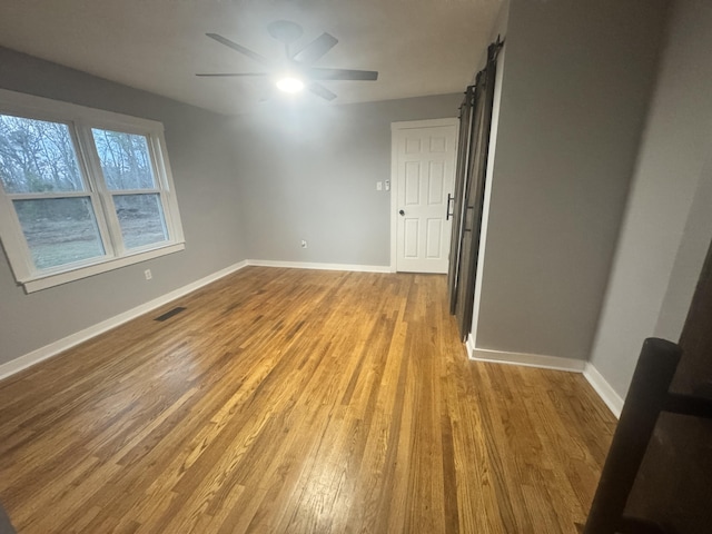 unfurnished room featuring baseboards, visible vents, light wood finished floors, and a barn door