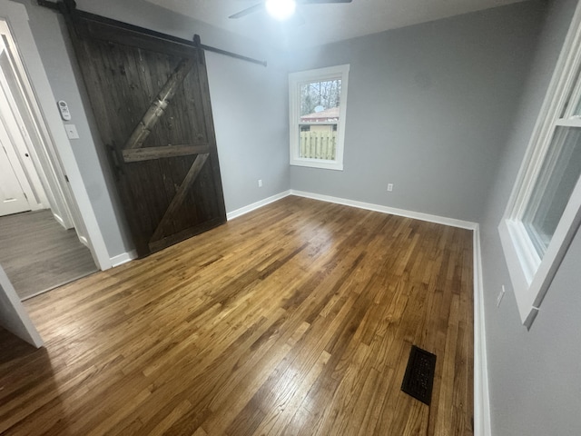 unfurnished bedroom featuring ceiling fan, a barn door, wood finished floors, and baseboards