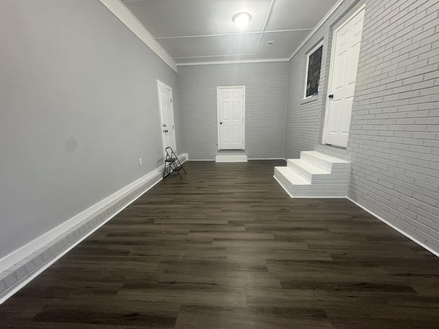 empty room with ornamental molding, brick wall, dark wood-type flooring, and baseboards