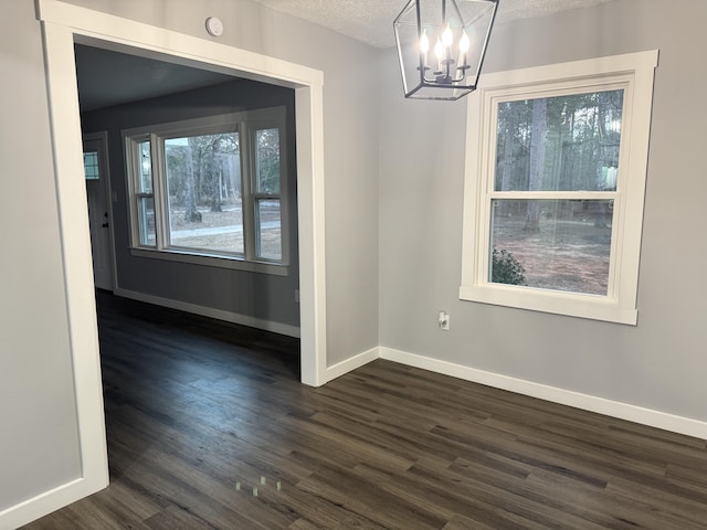 unfurnished dining area with a textured ceiling, dark wood-style flooring, and baseboards