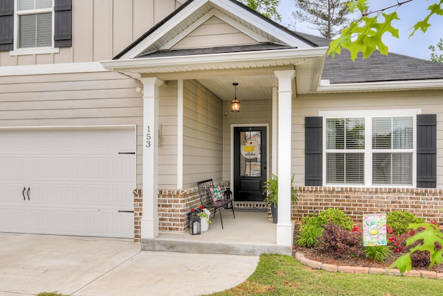 doorway to property featuring covered porch, brick siding, concrete driveway, and roof with shingles