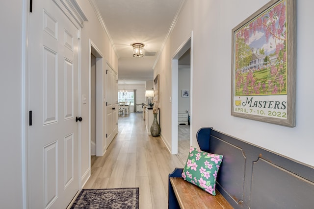 hallway with an inviting chandelier, ornamental molding, light wood-type flooring, baseboards, and visible vents