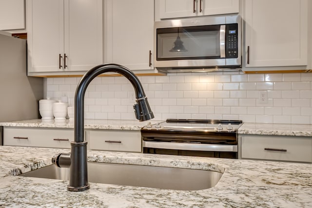 room details with light stone counters, stainless steel microwave, tasteful backsplash, and a sink