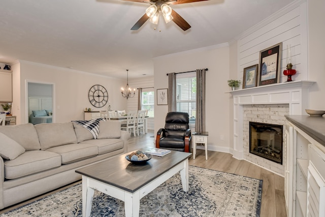 living area with a brick fireplace, crown molding, light wood-style flooring, and ceiling fan with notable chandelier