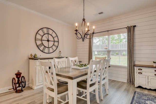 dining space with crown molding, wooden walls, a notable chandelier, and light wood-style flooring