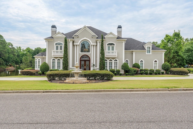 french country home with french doors, a balcony, and a front yard