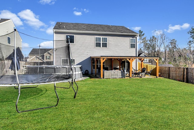 rear view of house with an outdoor living space, a patio, a yard, and a trampoline