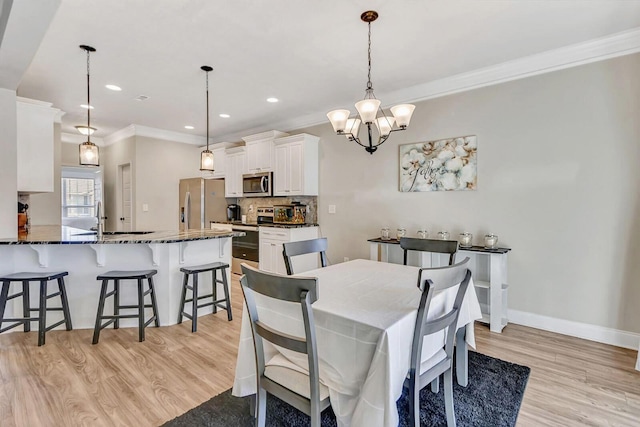 dining space featuring ornamental molding, sink, a chandelier, and light hardwood / wood-style floors