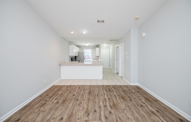 kitchen with light hardwood / wood-style flooring, stainless steel refrigerator, kitchen peninsula, and white cabinets