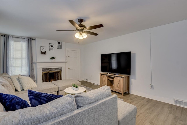 living room with ceiling fan, light hardwood / wood-style floors, and a premium fireplace