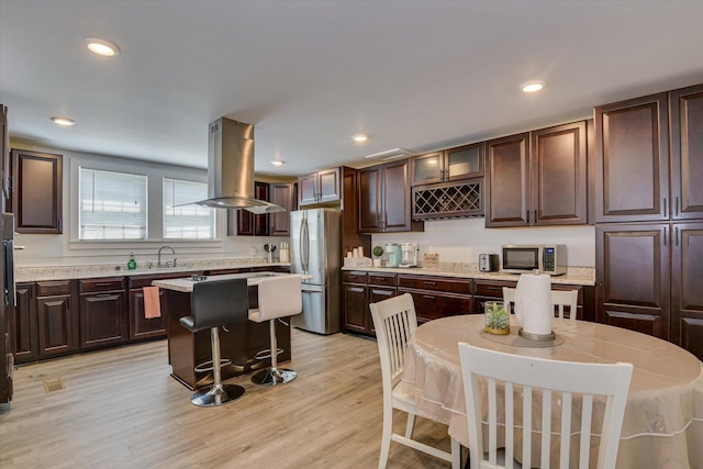 kitchen with dark brown cabinets, island range hood, stainless steel appliances, light hardwood / wood-style flooring, and a kitchen island