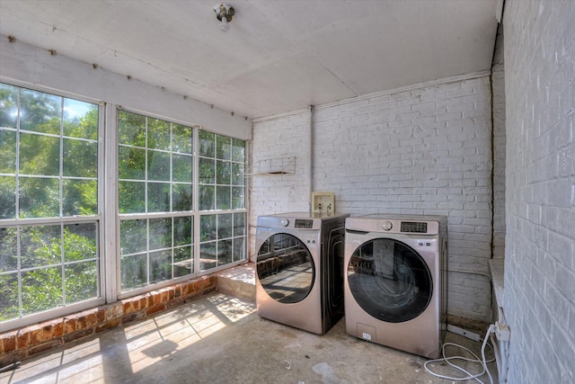 clothes washing area with washer and dryer and brick wall